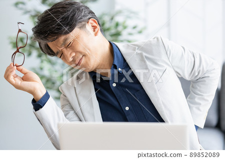一個身體不適的人,在辦公桌工作時把手放在背上 一個身體不適的人,在辦公桌工作時把手放在背上 89852089