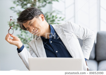 An unwell man who puts his hand on his back during desk work An unwell man who puts his hand on his back during desk work 89852090