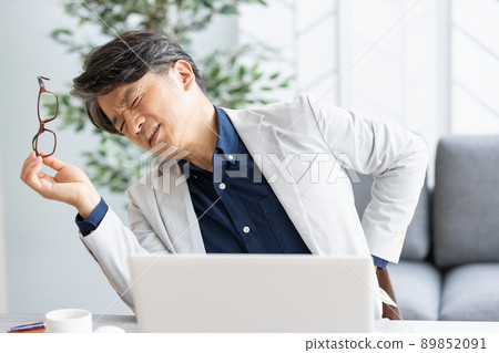 An unwell man who puts his hand on his back during desk work 89852091