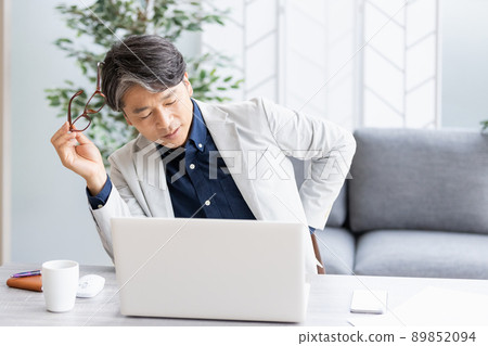 An unwell man who puts his hand on his back during desk work 89852094
