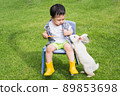 Asian cute boy sitting on a chair in the garden lawn holding carrots in hand and a white rabbit begging to eat.Happy day.Free time and holiday activities. 89853698