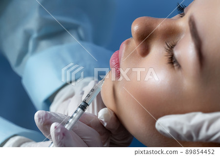 Hands of cosmetologist making injection in face, lips. Young woman gets beauty facial injections in salon. Face aging, rejuvenation and hydration procedures. Aesthetic cosmetology. 89854452