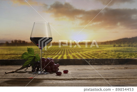 Still life with red wine glass and grapes on wooden table over background of panoramic view of lush vineyards at sunset. Tasting, festivals, country lifestyle and winemaking concept 89854453