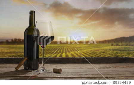 Charm. Still life with red wine glass and bottle on wooden table over background of panoramic view of lush vineyards at sunset. Tasting, festivals concept 89854459
