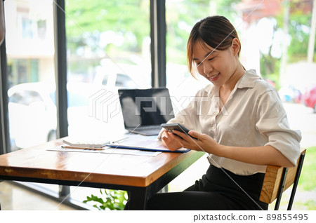 Female businesswoman using a smartphone in her bright workspace in the office. Female businesswoman using a smartphone in her bright workspace in the office. 89855495