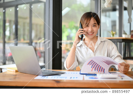 Female consultant talking on the phone with her client while reviewing financial report. Female consultant talking on the phone with her client while reviewing financial report. 89855497