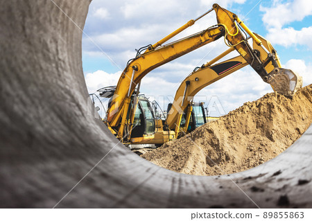 Heavy excavator at the construction site. View of the excavator through the iron pipe. Construction equipment for earthworks. Quarry excavator. 89855863