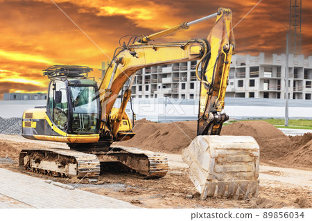 A heavy crawler excavator with a large bucket is getting ready for work against the sunset. Beautiful view of the excavator against the background of the sunset sky. Quarry excavators. 89856034