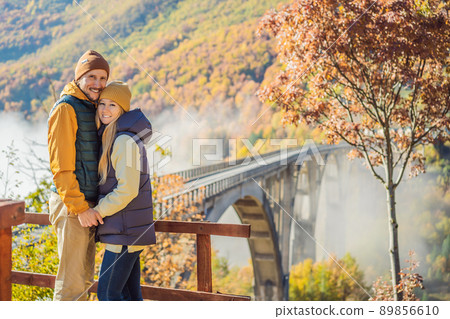 Montenegro. Happy couple man and woman in background of Dzhurdzhevich Bridge Over The River Tara foggy morning. Travel around Montenegro concept. Sights of Montenegro 89856610
