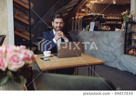 Attractive elegant successful man with coffee at laptop in luxury cafe smiling with chin on hands. Attractive elegant successful man with coffee at laptop in luxury cafe smiling with chin on hands. 89857839