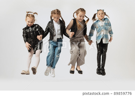 Happy school and preschool age children, beautiful girls jumping isolated on grey studio background. Beauty, kids fashion, education, happy childhood concept. 89859776