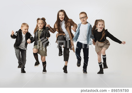 Happy school and preschool age children, girls and boys running, jumping isolated on grey studio background. Beauty, kids fashion, education, happy childhood concept. 89859780