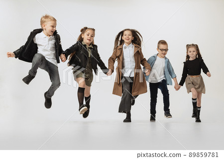 Happy school and preschool age children, girls and boys running, jumping isolated on grey studio background. Beauty, kids fashion, education, happy childhood concept. Happy school and preschool age children, girls and boys running, jumping isolated on grey studio background. Beauty, kids fashion, education, happy childhood concept. 89859781