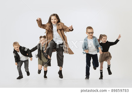 Emotional school and preschool age children, girls and boys running, jumping isolated on grey studio background. Beauty, kids fashion, education, happy childhood concept. 89859783