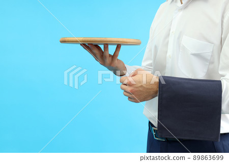 Young man waiter holds tray on blue background, space for text 89863699