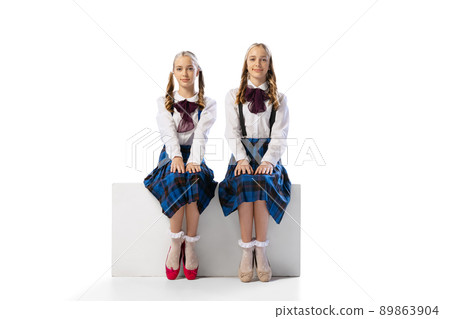 Portrait of two little girls, twins in retro costumes calmly sitting, posing isolated over white studio background 89863904