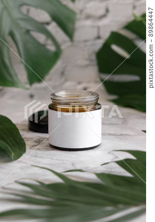 Brown jar and monstera leaves on marble table close up. Brand packaging mockup Brown jar and monstera leaves on marble table close up. Brand packaging mockup 89864447