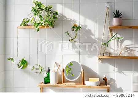 White tile wall with woonden shelves and comstics and green plants on them. Biophilic creative desing of bathroom. Home coomfort zone. Zero waste concept 89865214