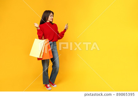 Attractive girl with paper bags and smartphone on yellow background Attractive girl with paper bags and smartphone on yellow background 89865395