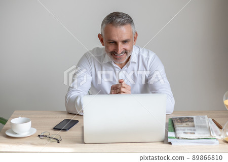Cheerful man looking at laptop sitting at table 89866810