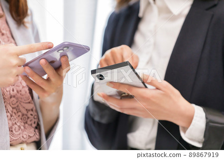 Two women looking at a smartphone, a colleague, synchronized 89867919