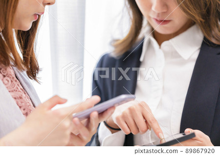Two women looking at a smartphone, a colleague, synchronized 89867920