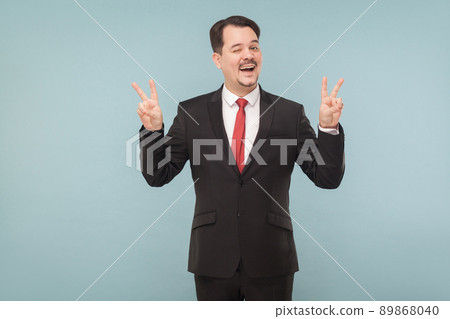 Businessman showing finger nomber four toothy smiling and wink. indoor studio shot. isolated on light blue background. handsome businessman with black suit, red tie and mustache looking at camera. Businessman showing finger nomber four toothy smiling and wink. indoor studio shot. isolated on light blue background. handsome businessman with black suit, red tie and mustache looking at camera. 89868040