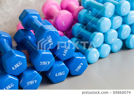 Blue and pink dumbbells lie on the gray floor. Studio shot Blue and pink dumbbells lie on the gray floor. Studio shot 89868074