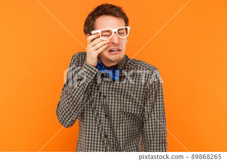Emotional man crying and wipes away tears. Studio shot. Isolated on orange background Emotional man crying and wipes away tears. Studio shot. Isolated on orange background 89868265