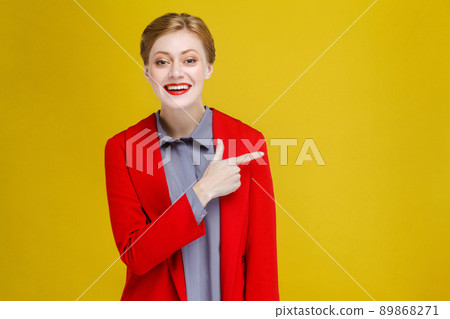 Redhead business woman in red suit showing at copy space. Studio shot, isolated on yellow background Redhead business woman in red suit showing at copy space. Studio shot, isolated on yellow background 89868271