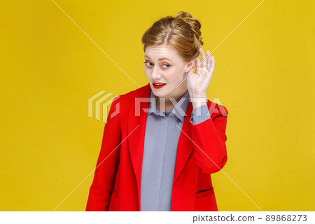 Ginger red head woman in red suit listening secret. Studio shot, isolated on yellow background Ginger red head woman in red suit listening secret. Studio shot, isolated on yellow background 89868273
