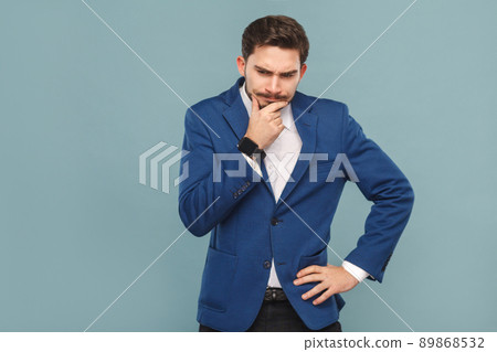 Let's me think. Pondering young adult man touching chin . Business people concept, richly and success. Indoor, studio shot on light blue background 89868532