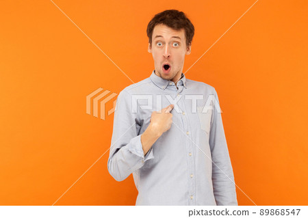 Shocked man looking at camera and pointing finger himself. Studio shot, orange background Shocked man looking at camera and pointing finger himself. Studio shot, orange background 89868547