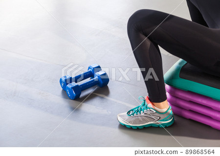 Closeup legs, sneakers,step platform and dumbbells. Woman sit. Studio shot 89868564