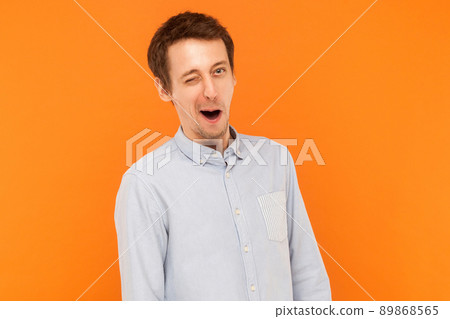 Emotional businessman wearing blue shirt, wink at camera. Indoor shot, orange background 89868565