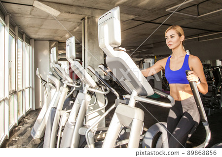 Blonde sporty woman in fitness club or gym, ride on orbitrack. Studio shot 89868856