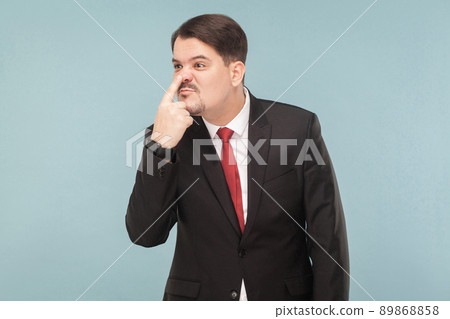 From your lies I see how your nose grows like a pinocchio. indoor studio shot. isolated on light blue background. handsome businessman with black suit, red tie and mustache looking away. 89868858