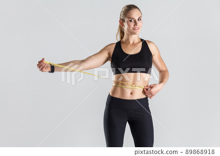 Weight loss. Ideal figure. Happiness girl holding centimeter and smiling. Studio shot, gray background Weight loss. Ideal figure. Happiness girl holding centimeter and smiling. Studio shot, gray background 89868918