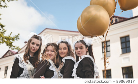Cheerful Russian girls graduating with orange balloons on the last school day. 89869017