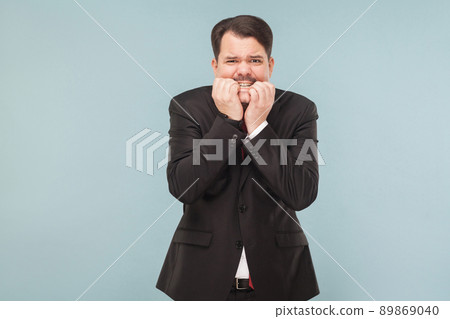 Worry business man bites his nails with excitement. indoor studio shot. isolated on light blue background. handsome businessman with black suit, red tie and mustache looking at camera nervous. Worry business man bites his nails with excitement. indoor studio shot. isolated on light blue background. handsome businessman with black suit, red tie and mustache looking at camera nervous. 89869040