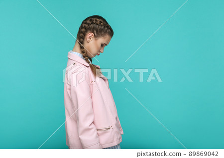 profile side view of sad unhappy depressed portrait of beautiful cute girl standing with makeup and brown pigtail hairstyle in pink jacket. indoor, studio shot isolated on blue or green background. profile side view of sad unhappy depressed portrait of beautiful cute girl standing with makeup and brown pigtail hairstyle in pink jacket. indoor, studio shot isolated on blue or green background. 89869042