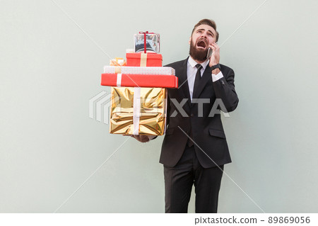 Angry businessman holding gift box and shout at phone. Studio shot, gray background Angry businessman holding gift box and shout at phone. Studio shot, gray background 89869056