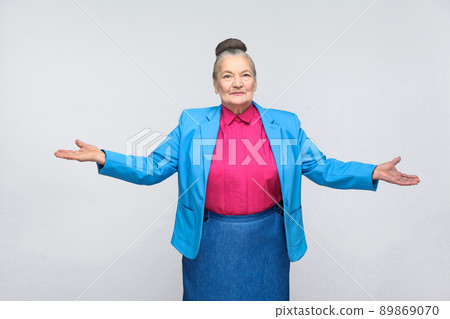 Welcome my dear! Happiness woman looking at camera. Emotion and feelings concept. Portrait of handsome expressive grandmother standing with collected gray hair. Studio shot isolated on gray background Welcome my dear! Happiness woman looking at camera. Emotion and feelings concept. Portrait of handsome expressive grandmother standing with collected gray hair. Studio shot isolated on gray background 89869070