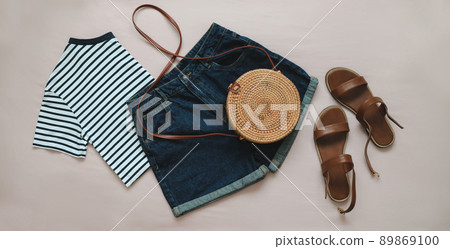 flat lay composition with female top, denim shorts, sandals and a wicker rattan bag on beige background top view 89869100