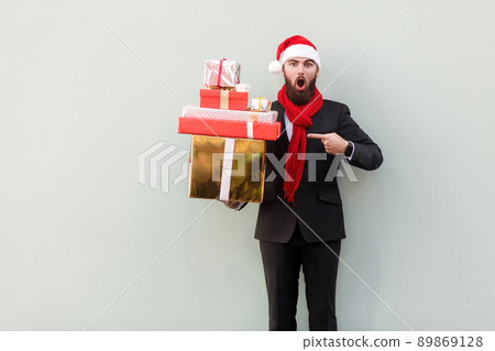 Amazed businessman pointing finger on many colorful gift box and looking at camera with open mouth and big eyes. Studio shot 89869128