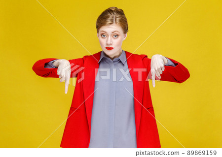 Ginger red head woman in red suit wish pointing down at copy space. Studio shot, isolated on yellow background Ginger red head woman in red suit wish pointing down at copy space. Studio shot, isolated on yellow background 89869159