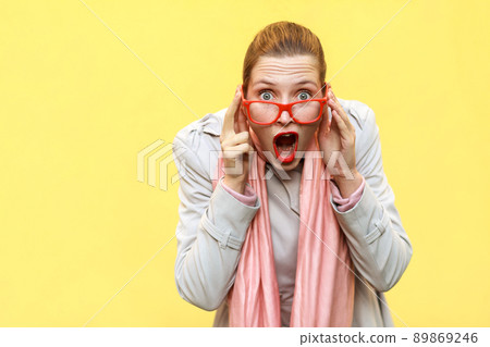 Shocked woman wearing coat, pink scarf, opening mouths , having surprised shocked face. Studio shot 89869246