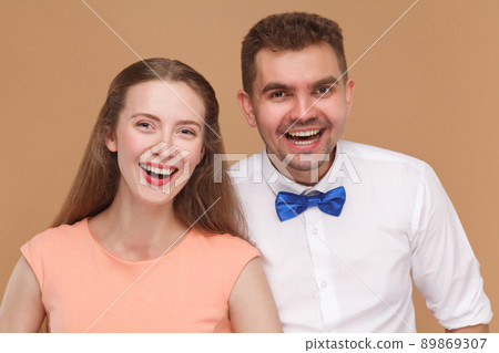 closeup portrait of happy handsome man and beautiful blonde woman or young couple standing together, looking at camera with toothy joyful smile. indoor studio shot, isolated on light brown background closeup portrait of happy handsome man and beautiful blonde woman or young couple standing together, looking at camera with toothy joyful smile. indoor studio shot, isolated on light brown background 89869307