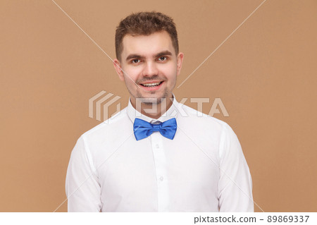 Perfect man in blue bow of tie toothy smiling . Business people concept, good and bad emotion and feelings. Studio shot, isolated on light brown background 89869337