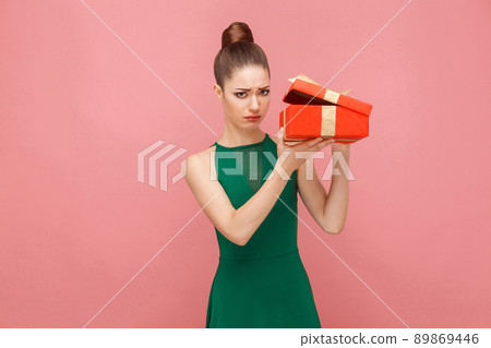 Woman unboxing red gift box looking inside, ahve sadness look. Expression emotion and feelings concept. Studio shot, isolated on pink background Woman unboxing red gift box looking inside, ahve sadness look. Expression emotion and feelings concept. Studio shot, isolated on pink background 89869446